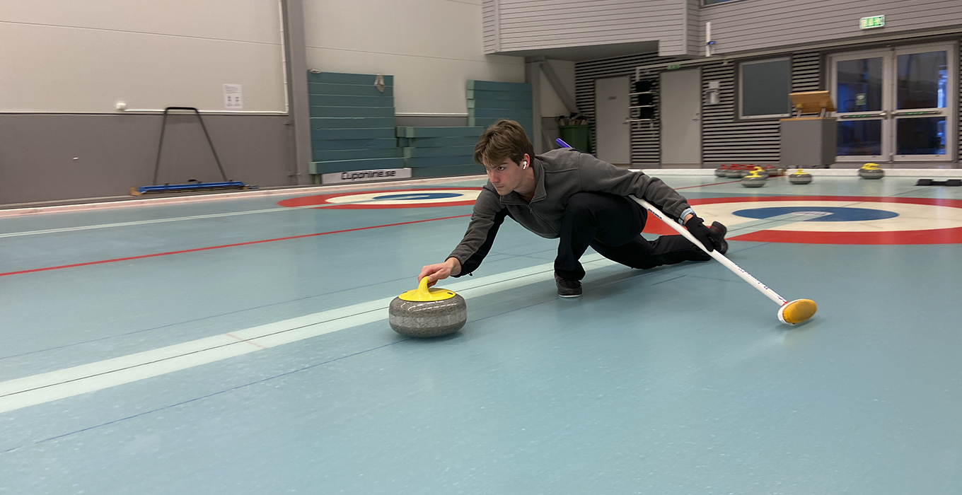 sju barn sitter på rad på is med varsin curlingsten